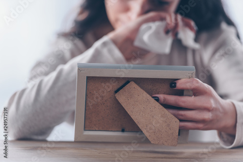 cropped view of upset woman holding picture frame and crying at home photo