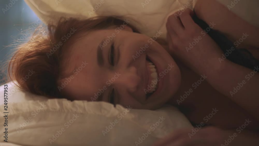 Pretty woman with adorable smile looking in camera lying in bed close up. Shooting under the blanket Pretty woman with adorable smile looking in camera lying in bed close up. Shooting under the blanket