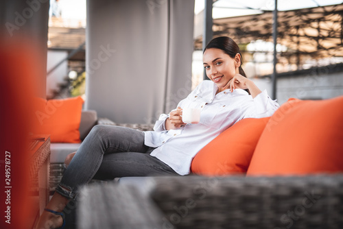 Pretty young lady smiling to the camera while sitting with coffee