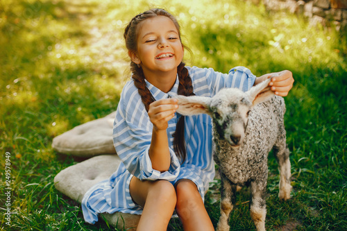beautiful and cute girl in blue dresses with beautiful hairstyles and make-up sitting in a sunny green garden and playing with a goat