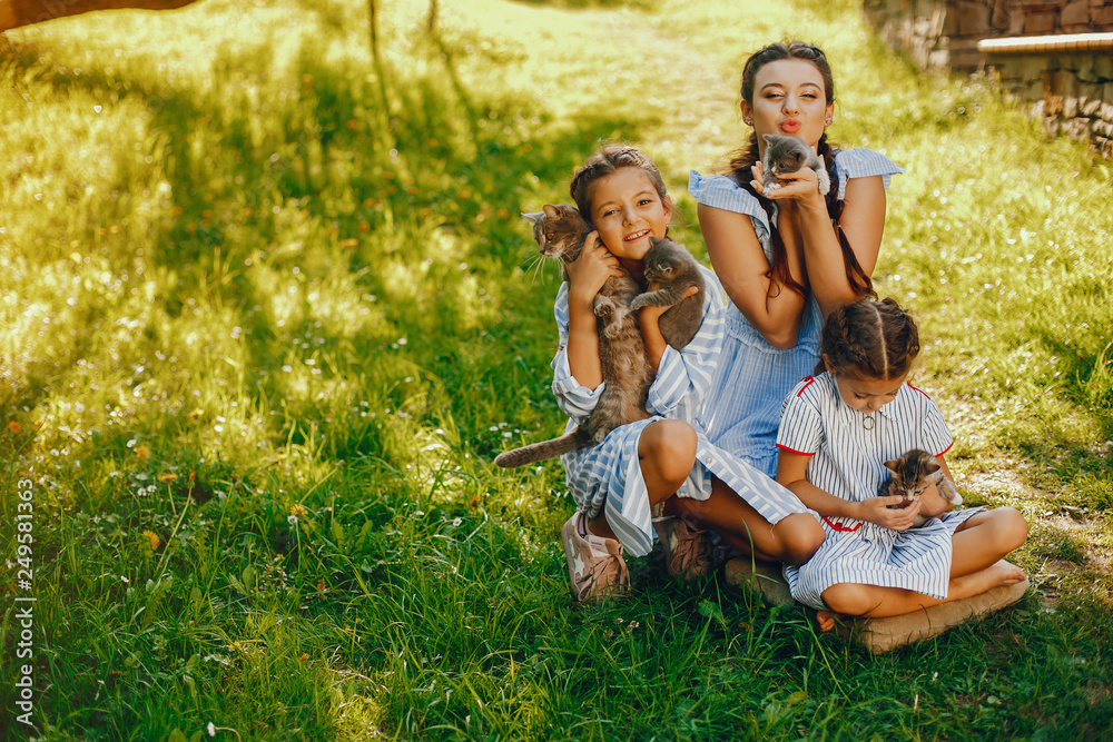 three beautiful and cute girls in blue dresses with beautiful hairstyles and make-up sitting in a sunny green garden and playing with a cats three beautiful and cute girls in blue dresses with beautiful hairstyles and make-up sitting in a sunny green garden and playing with a cats