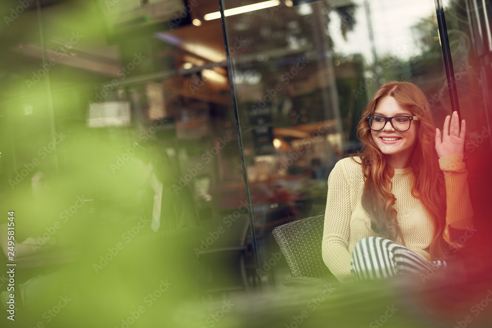 Attractive red-haired girl in glasses showing hello gesture in cafe Attractive red-haired girl in glasses showing hello gesture in cafe