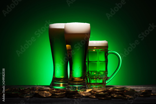 glasses of irish beer standing near golden coins on table on green background