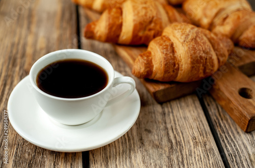 coffee and croissants on wooden cutting board, on wooden background