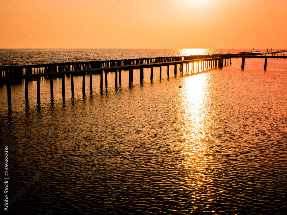 Low tide during sunset silhouette wooden pole and bridge through the sea beautiful orange sky background of nature