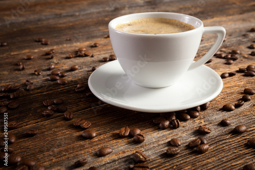 White cup of coffee with several coffee beans on standing on a vintage wooden table