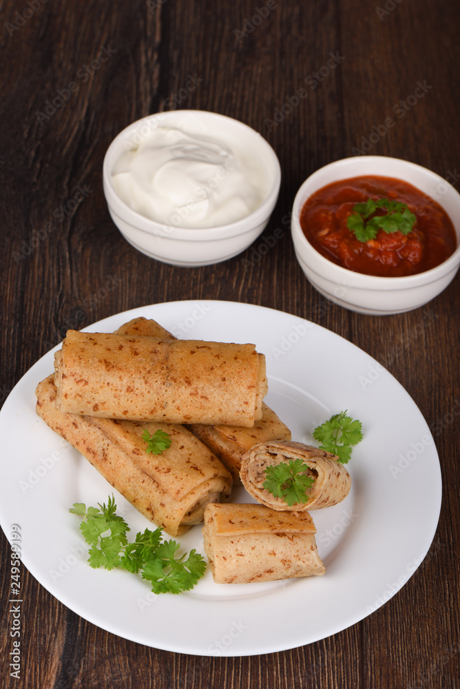 Pancake rolls with meat filling, served with fresh parsley, sour cream and ketchup sauce Pancake rolls with meat filling, served with fresh parsley, sour cream and ketchup sauce