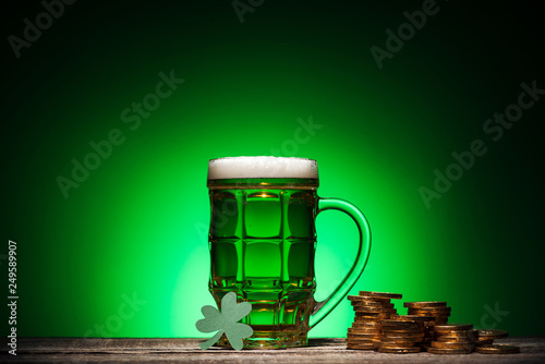 glass of green irish beer near golden coins and cube calendar on green background