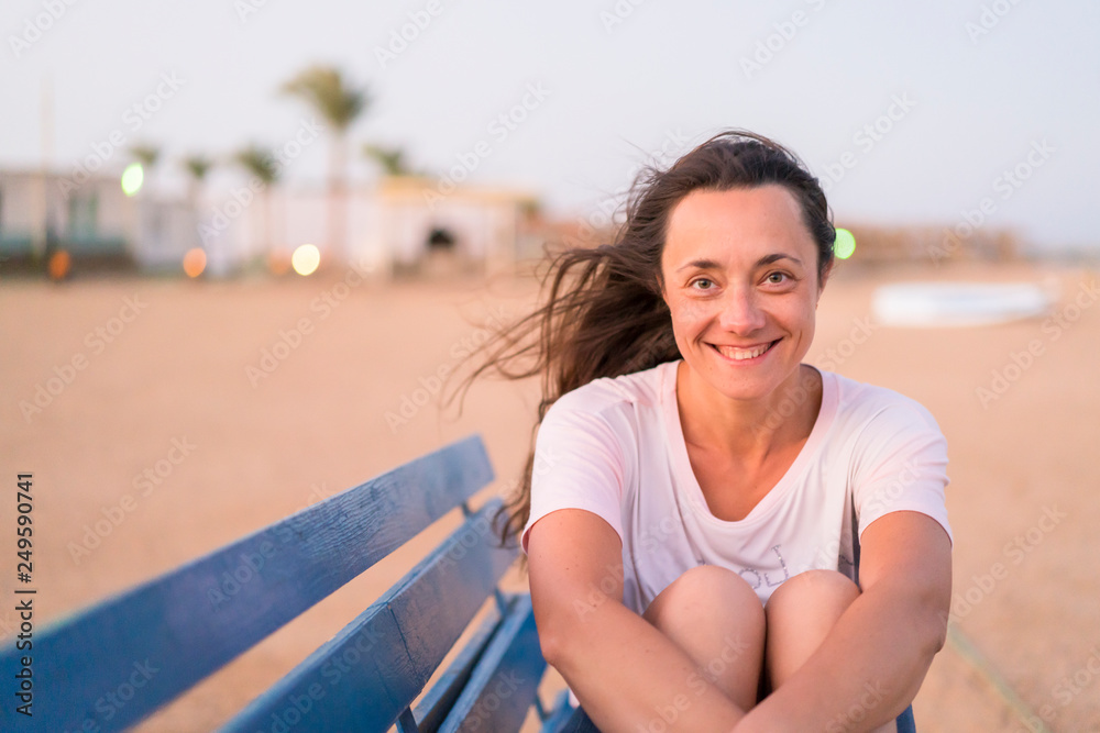 Young woman resting on bench. A woman with a beautiful smile on a blue bench. The concept of rest and happiness. copy space