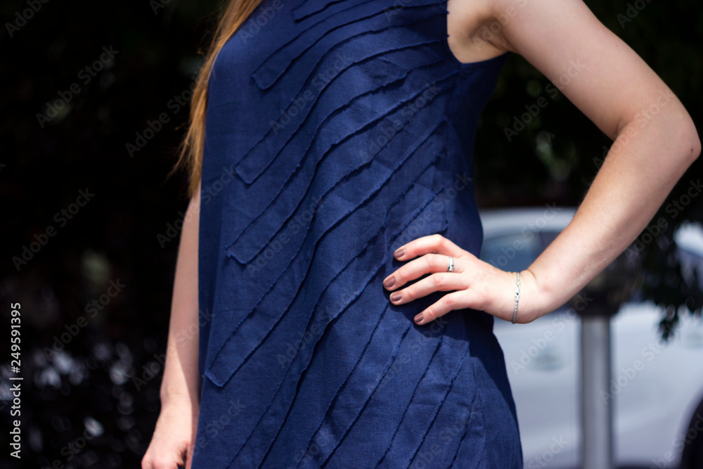Young woman in dark blue linen dress standing on sidewalk, fashion and style