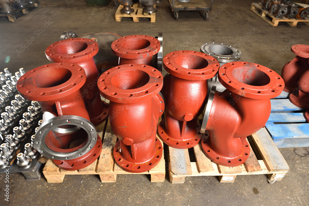 Large metal or cast iron pipes, bases for creating valves, lie on a wooden panel before further processing on a milling machine. Red bases to create valves in the factory. Big Red valves factory