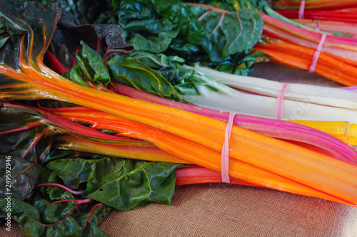 Bunches of rainbow Swiss chard with bright red  and orange stalks and green leaves for sale at a farmers market 