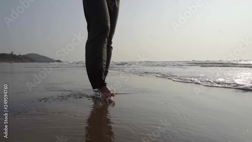 lonely woman is strolling over seashore, stepping in waves, detail view of legs photo