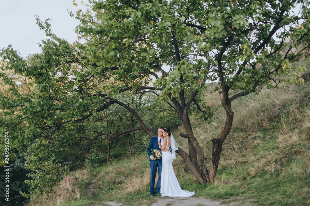 Newlyweds in love hugging in the fall against the background of green maidens in the garden. Portrait of a stylish groom with glasses and a cute bride in a white palette. Wedding photography. Newlyweds in love hugging in the fall against the background of green maidens in the garden. Portrait of a stylish groom with glasses and a cute bride in a white palette. Wedding photography.