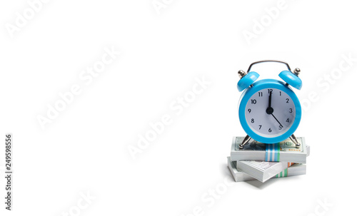 A clock is standing on a bunch of packs of money on a white background. The concept of expressing time is money. Planning time and increase efficiency, increase profits. Side job in free time.