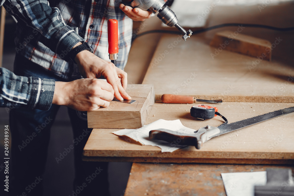 A man carves a tree. The carpenter works with a drill in a studio. An engineer provides a tree shape