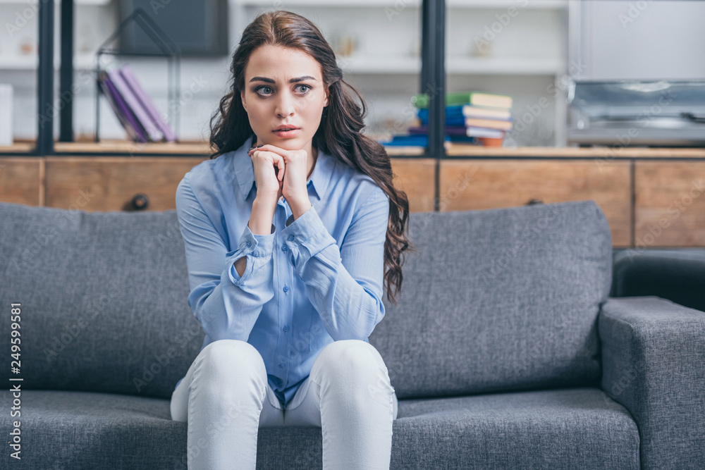 sad woman in blue blouse and white pants sitting on grey couch in kitchengrieving disorder concept , sad woman in blue blouse and white pants sitting on grey couch in kitchengrieving disorder concept ,