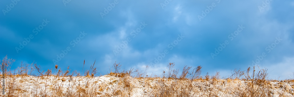 Obraz premium hill covered with snow and dry grass against the blue sky.