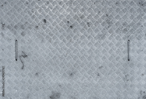 View from above of a galvanized, rectangular manhole cover made of checker plate with two handles, used in a workshop photo