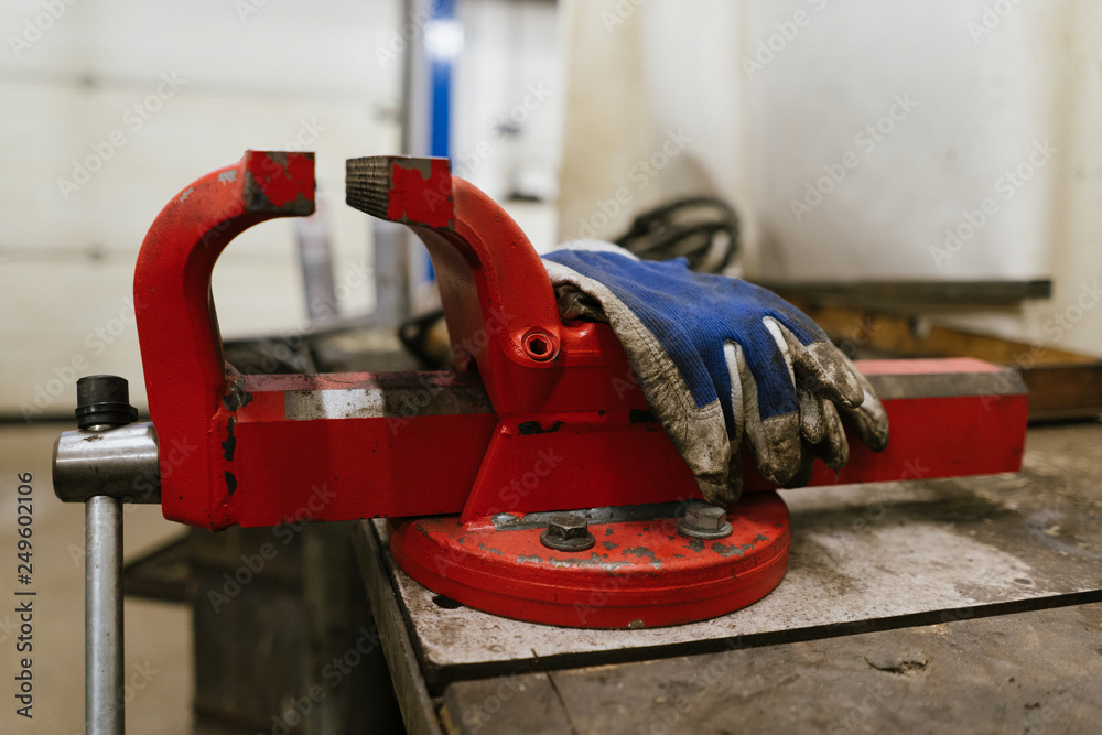 Red vise, taken from the side, with dirty blue protective gloves over it, in a garage of a car repair shop