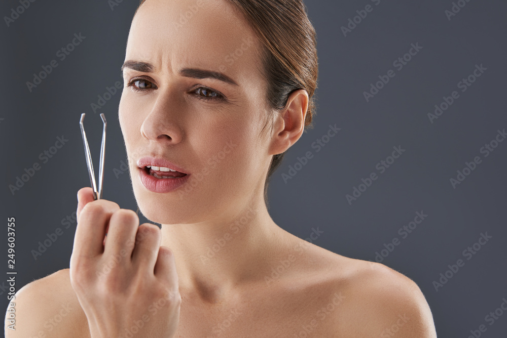 Obraz premium Lovely young woman looking at on tweezer in her hands