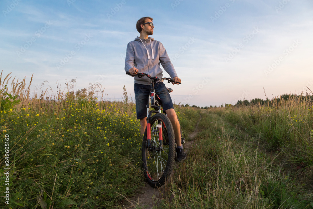 Young man on bicycle, cyclist in field with green grass and flowers, beautiful nature landscape, copy space