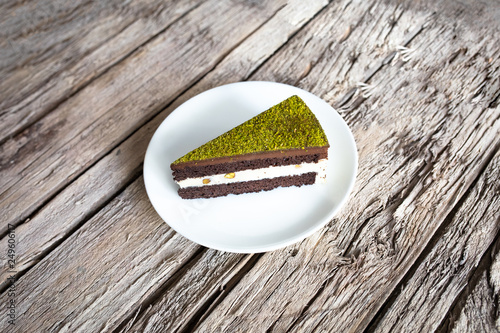 A piece of yummy delicious chocolate and creamy cake with pistachios in white plate on wooden surface table. Slice of chocolate cake
