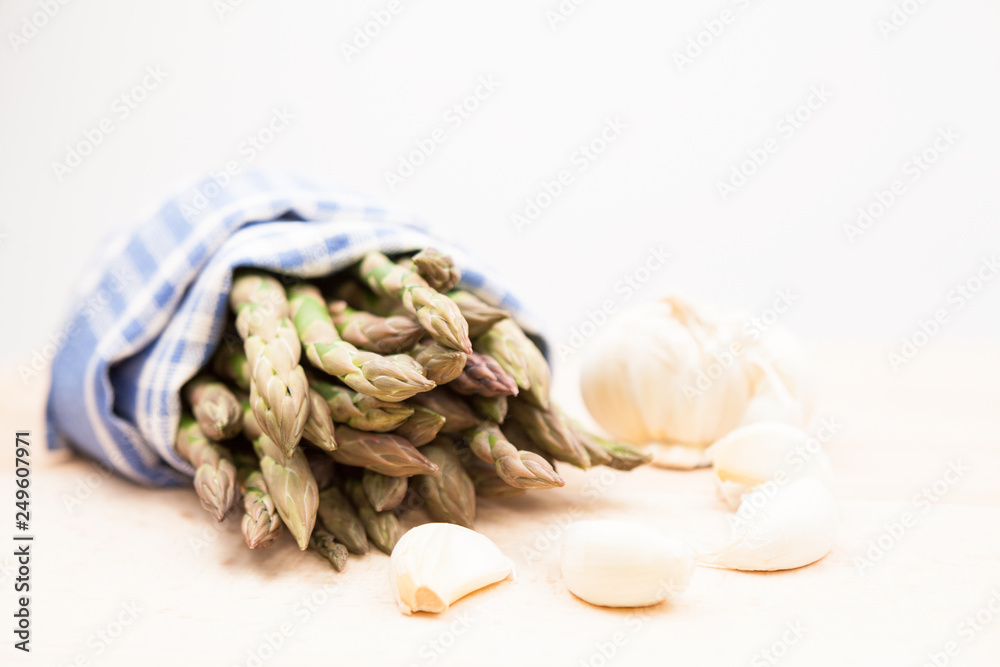 Fresh asparagus stems in a blue and white textile napkin and garlic Fresh asparagus stems in a blue and white textile napkin and garlic