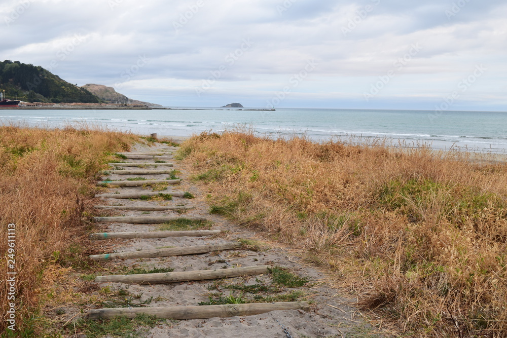 The sandy path leads up the beach towards the shore with a island of land in the distant waves in Gisborne, New Zealand.