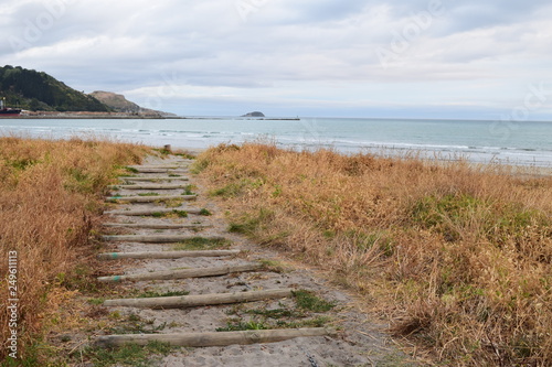 The sandy path leads up the beach towards the shore with a island of land in the distant waves in Gisborne  New Zealand.