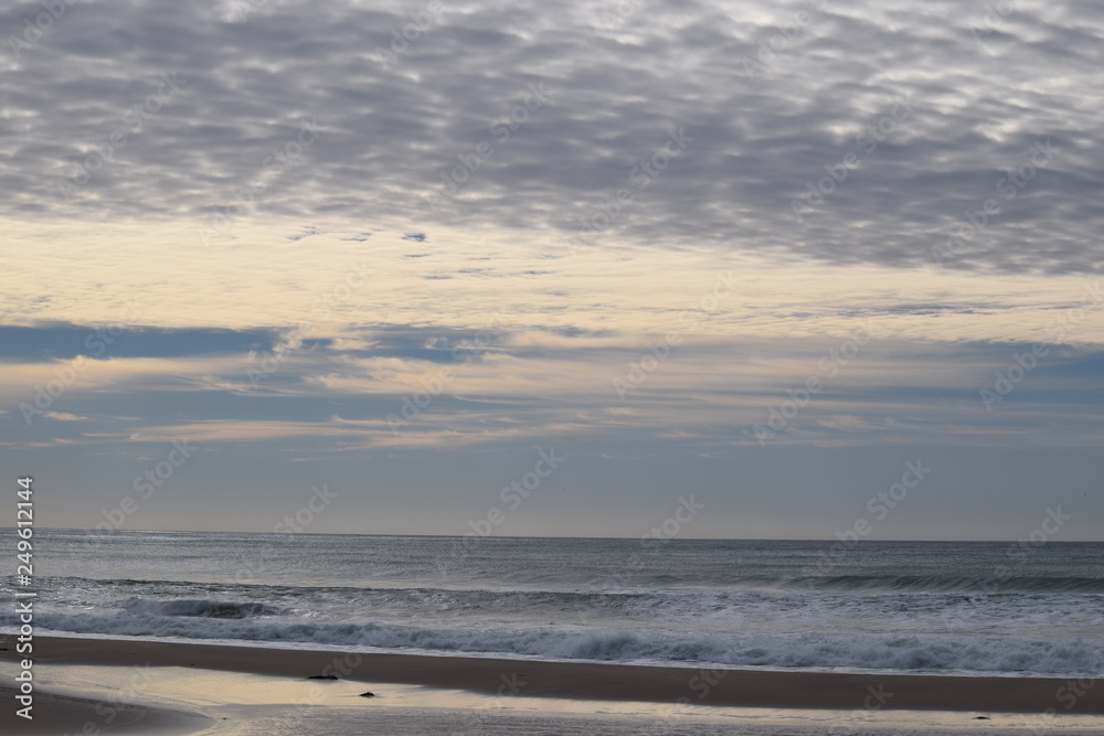 The waves in the calm sea meet the patterned cloud in the morning sky in Gisborne, New Zealand.