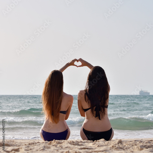 Two girls on the beach holding each others hands to form a heart shape
