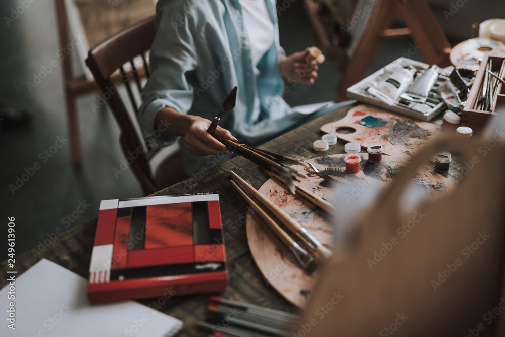 Female artist with spatula taking paintbrushes from the table Female artist with spatula taking paintbrushes from the table