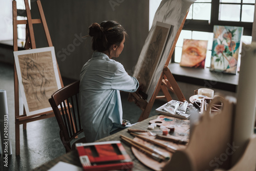 Female artist turning to the canvas while sitting at the table © Yakobchuk Olena