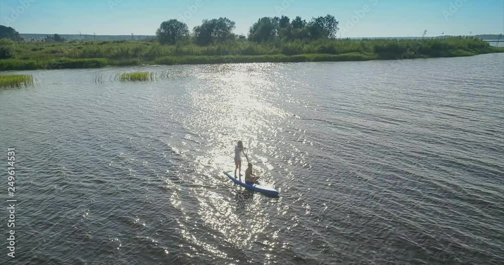 Two girls on the paddle board are floating on the river at sunset Two girls on the paddle board are floating on the river at sunset
