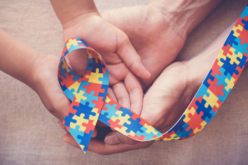 Hands holding puzzle ribbon for autism awareness