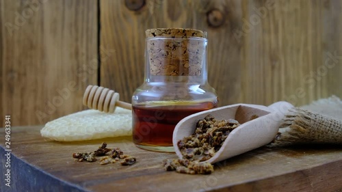 A bottle of propolis tincture and a wooden scoop of propolis granules. Medical preparations bee propolis. Bee glue. Apitherapy. How to treat bee products.