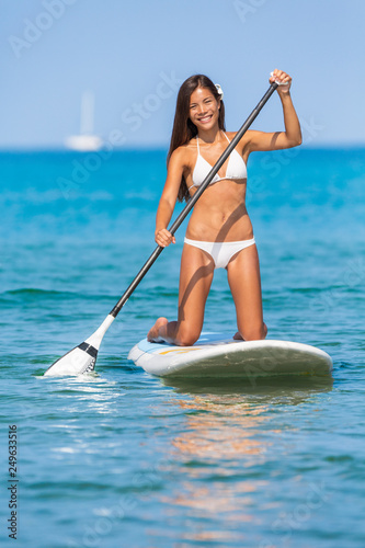Paddleboard SUP Asian girl having fun paddle board in Hawaii. Fitness recreational leisure activity. Beach rental equipment on travel vacation. Bikini Chinese multiracial woman.