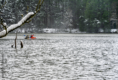 Woman and man are kayaking on winter snow-covered lake in the forest