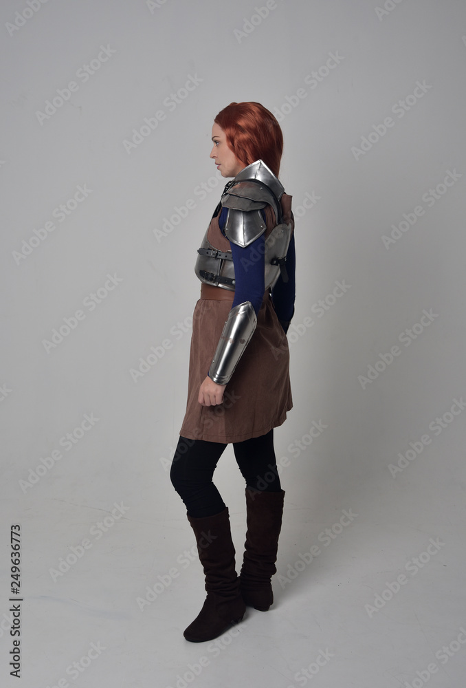 full length portrait of a red haired girl wearing medieval warrior costume and steel armour, standing pose on grey studio background. full length portrait of a red haired girl wearing medieval warrior costume and steel armour, standing pose on grey studio background.
