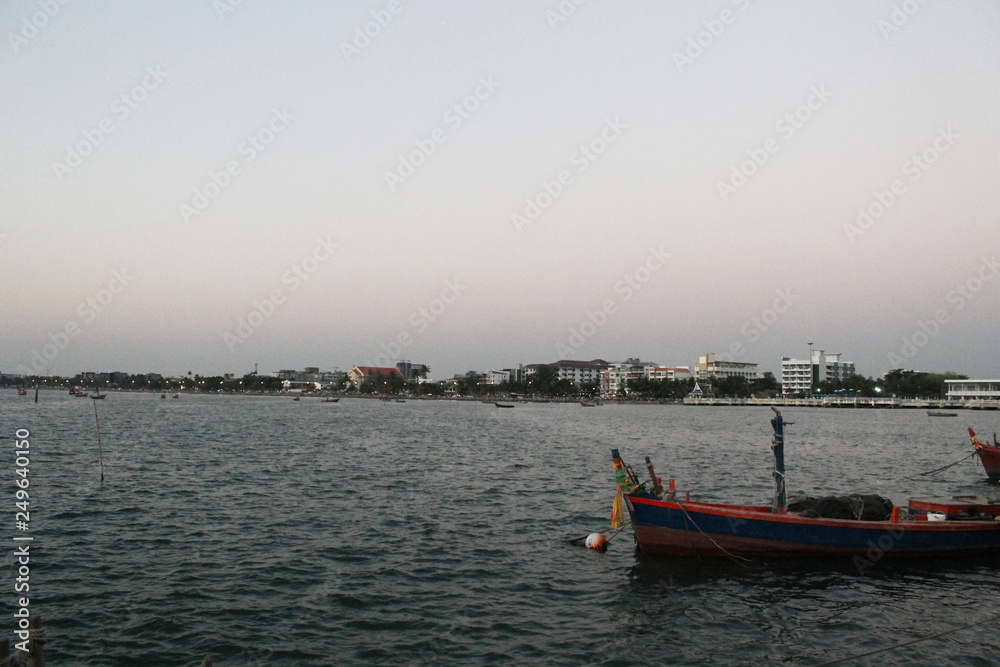 Naklejka premium fishing boat in the sea and sunset sky and city background