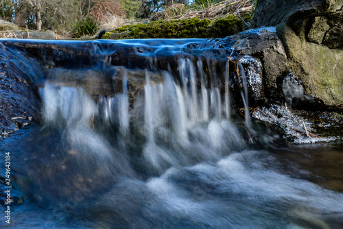 Fototapeta Naklejka Na Ścianę i Meble -  water running down the cascading creek inside park on a sunny cold winter morning 