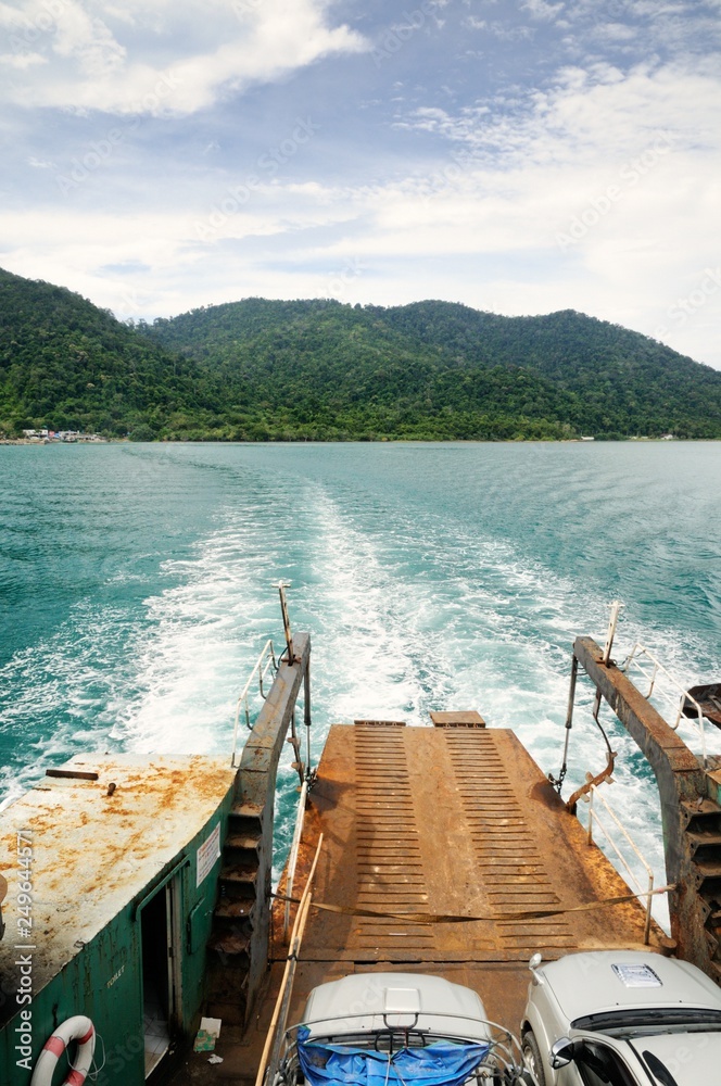 Ferry ramp and trace on the water of tropical sea behind ferry, with tropical Koh Chang island on horizon in Thailand