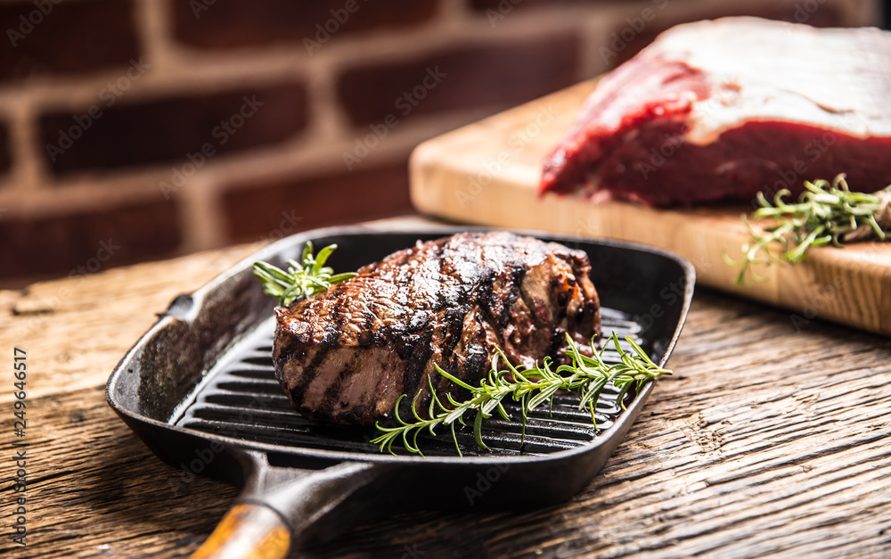 Grilled beef steak in grill pan with herbs rosemary on wooden table