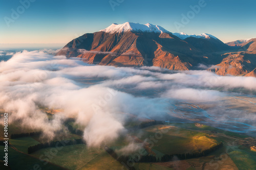 The valley is flooded in mist in a mountain environment. Over the fogs, only the high peaks of the mountains rise beneath the sunny sky. Misty morning on the Southern Island New Zealand, Christchurch