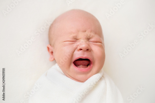 Newborn baby boy on a white background. Baby is crying