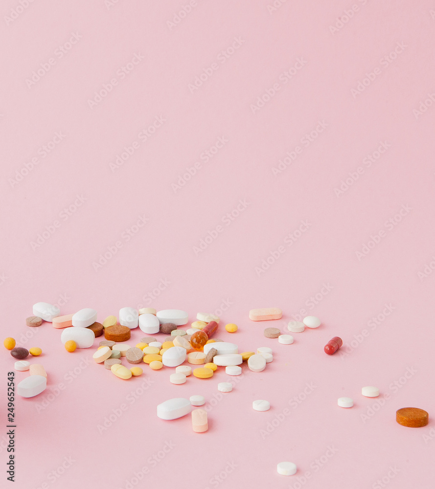 group of capsules and pills in different colors and shape isolated on pink background