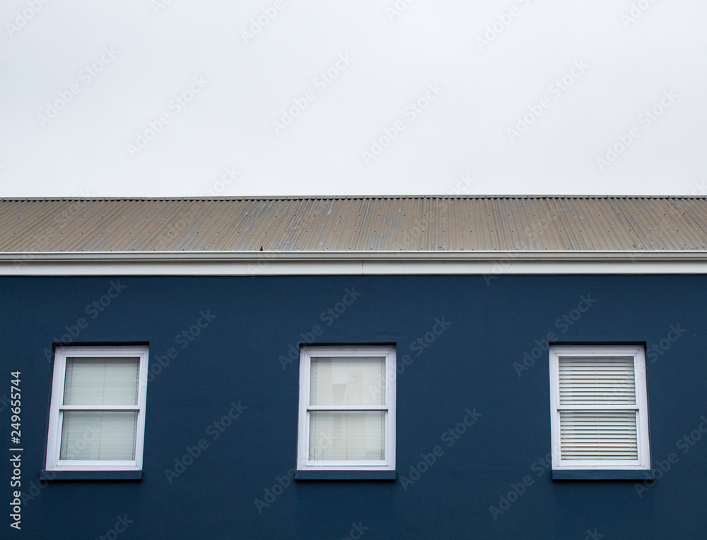 A game of tones and geometries: blue house, white windows, grey sky A game of tones and geometries: blue house, white windows, grey sky