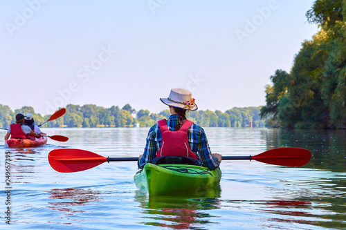 Woman in elegant straw hat canotier paddling green kayak at Danube river at summer. Concept of recreation and adventure