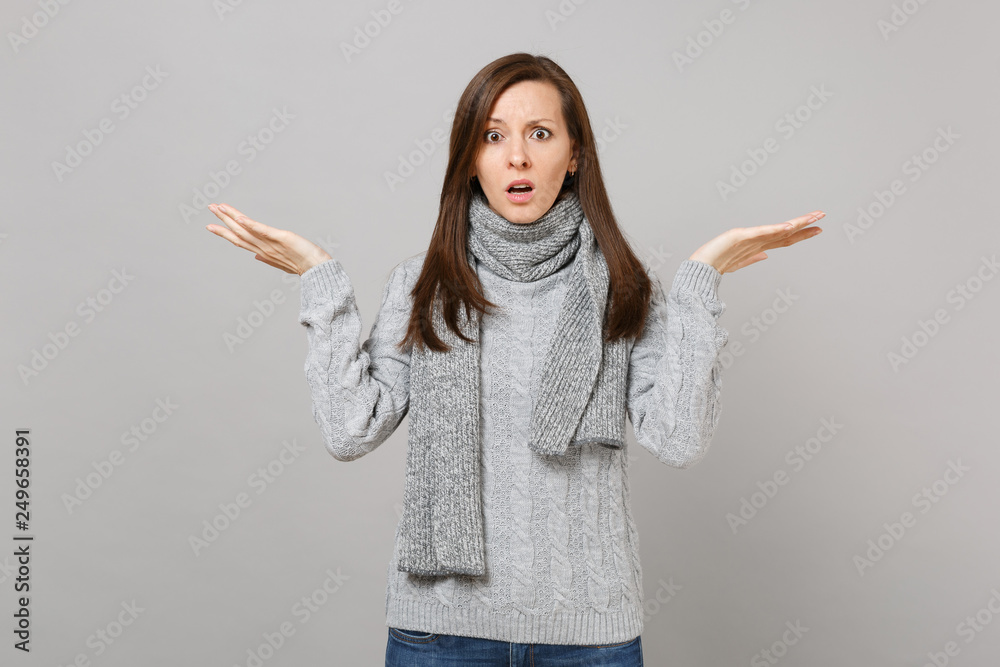Shocked puzzled young woman in gray sweater scarf spreading hands isolated on grey wall background in studio. Healthy fashion lifestyle people sincere emotions cold season concept. Mock up copy space. Shocked puzzled young woman in gray sweater scarf spreading hands isolated on grey wall background in studio. Healthy fashion lifestyle people sincere emotions cold season concept. Mock up copy space.